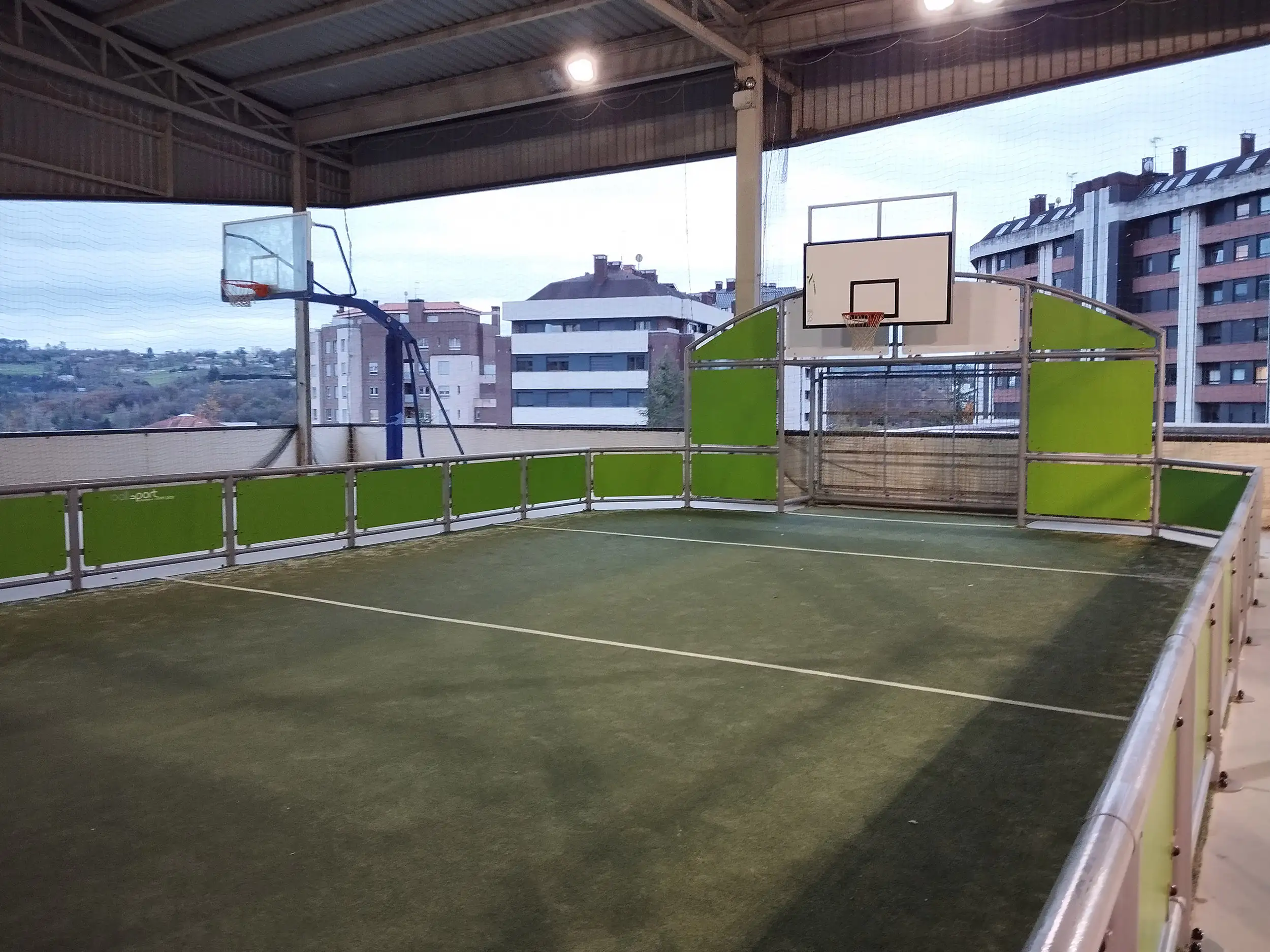 Pistas exteriores de baloncesto cubiertas, con canastas. Vista de edificios al fondo