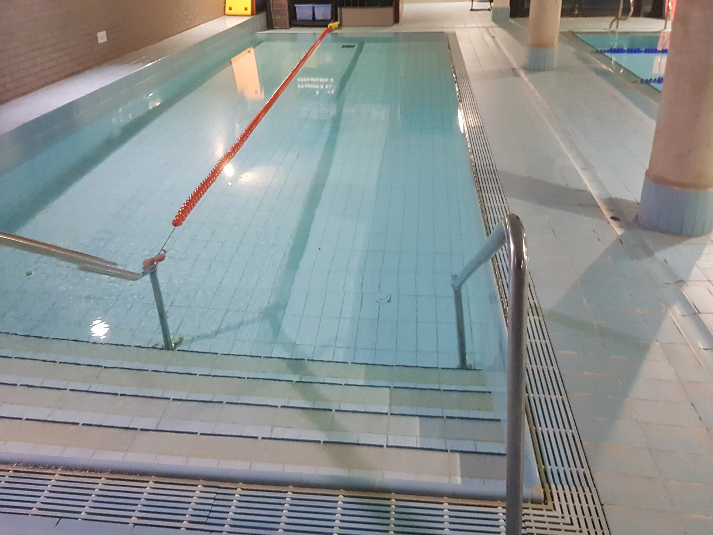 Piscina de aprendizaje climatizada, con las escalerillas de acceso en primer plano y una cuerda de seguridad