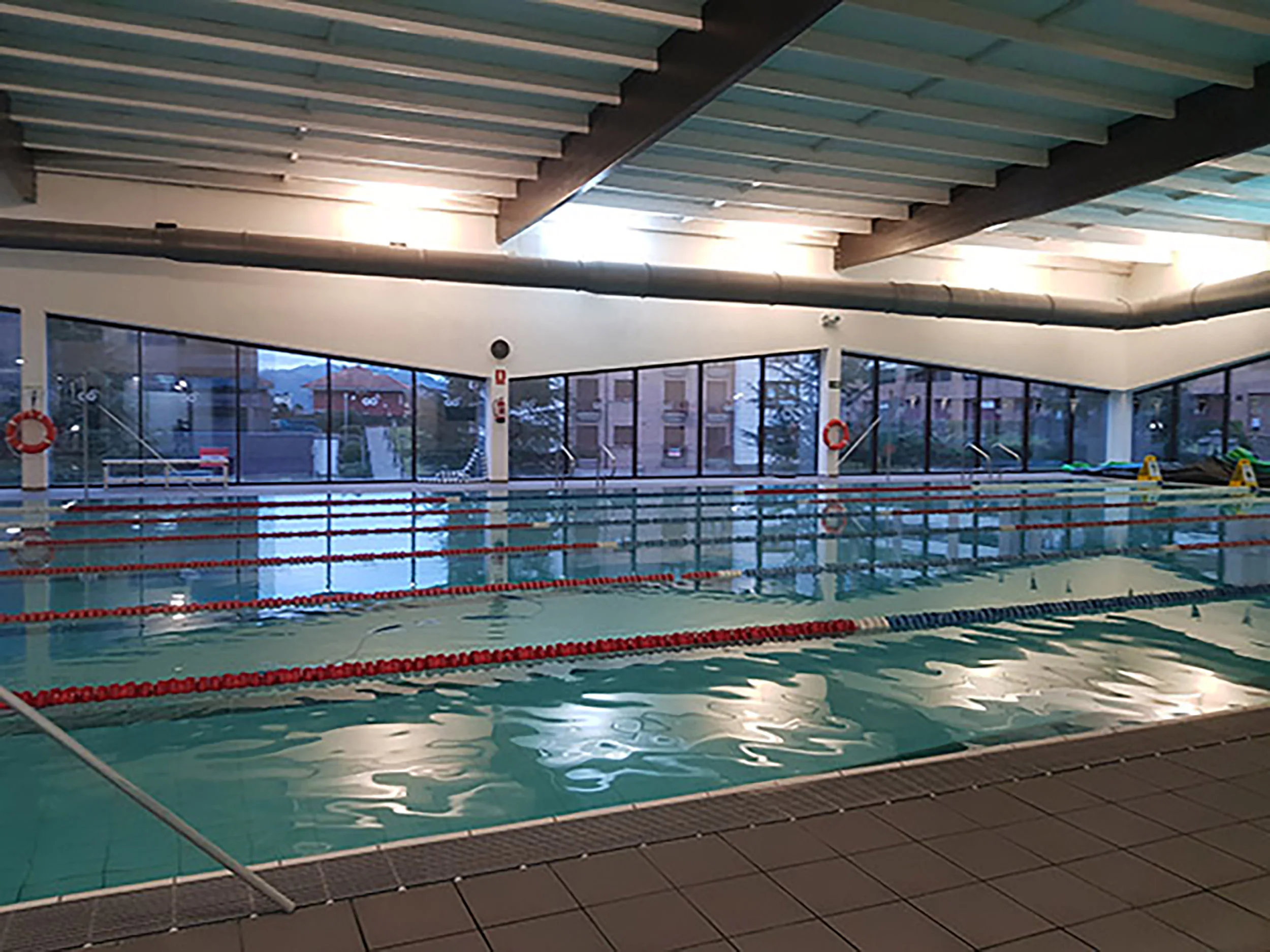 Panorámica lateral de la piscina de nado, con amplios ventanales con vistas al exterior