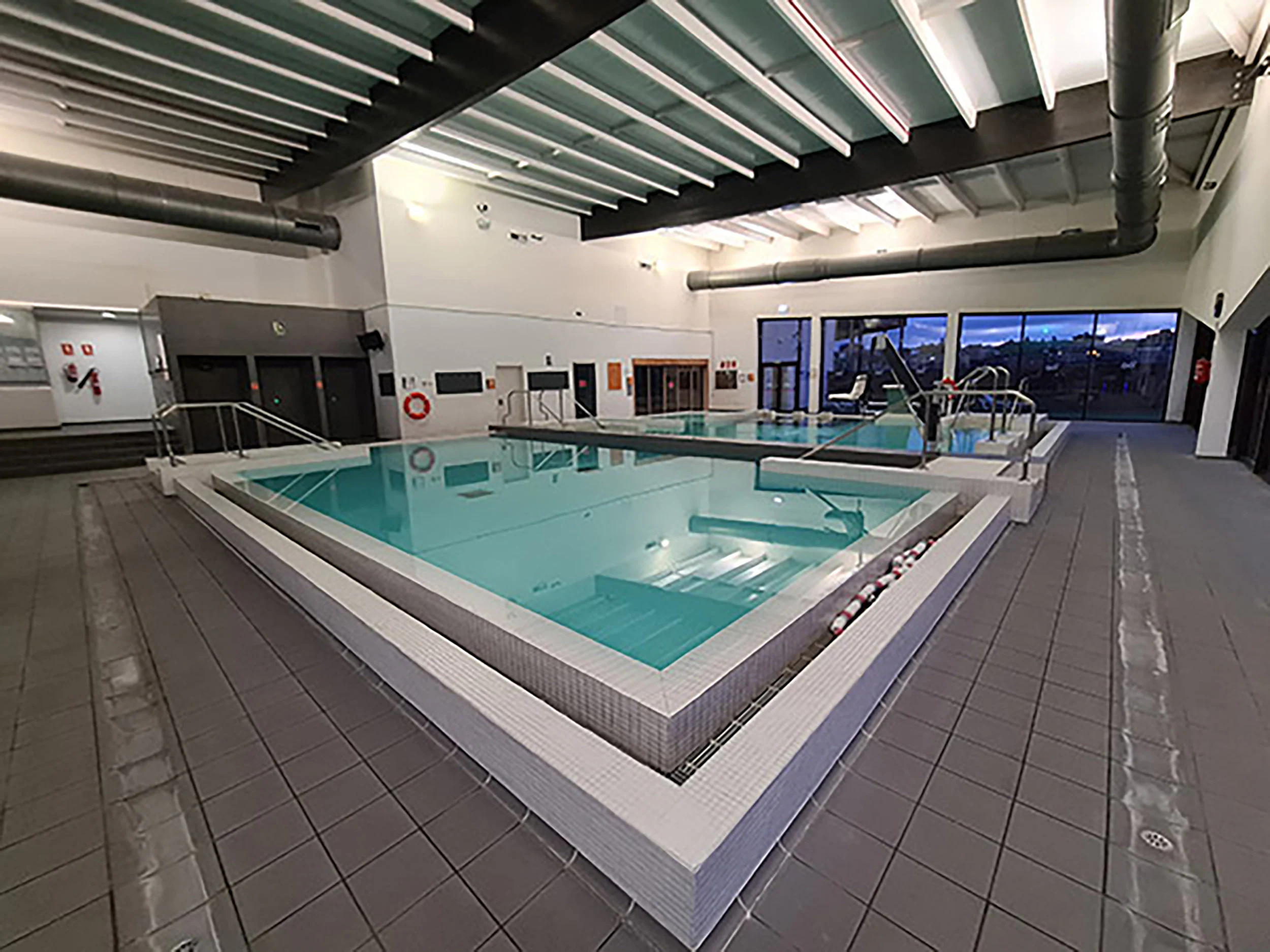 Piscinas de aprendizaje y spa, con escalerillas, barandillas de acceso y ventanales al fondo