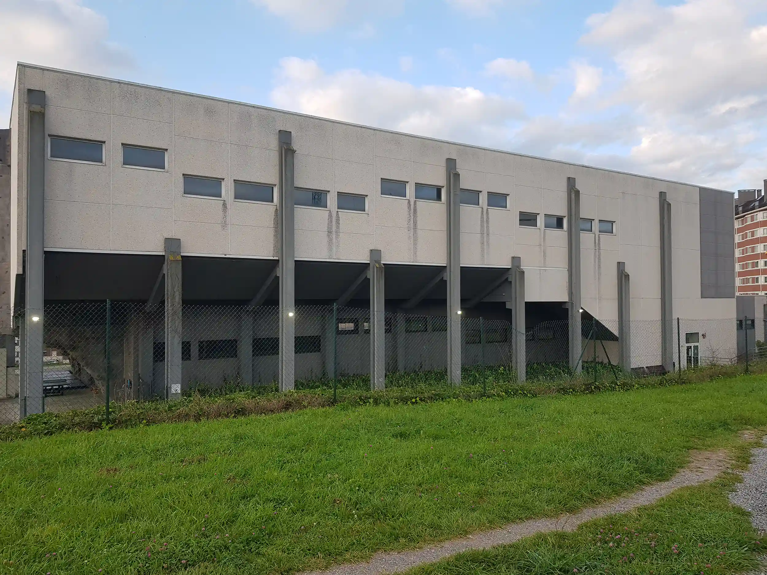 Vista lateral del exterior del edificio, con un pasillo bajo sus columnas y césped exterior