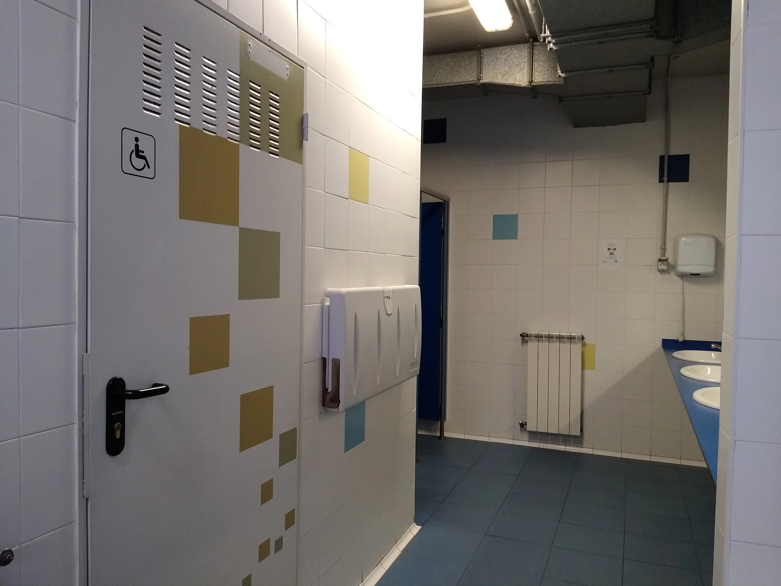 Detalle de los aseos, con vista de la puerta de entrada al aseo para personas con discapacidad