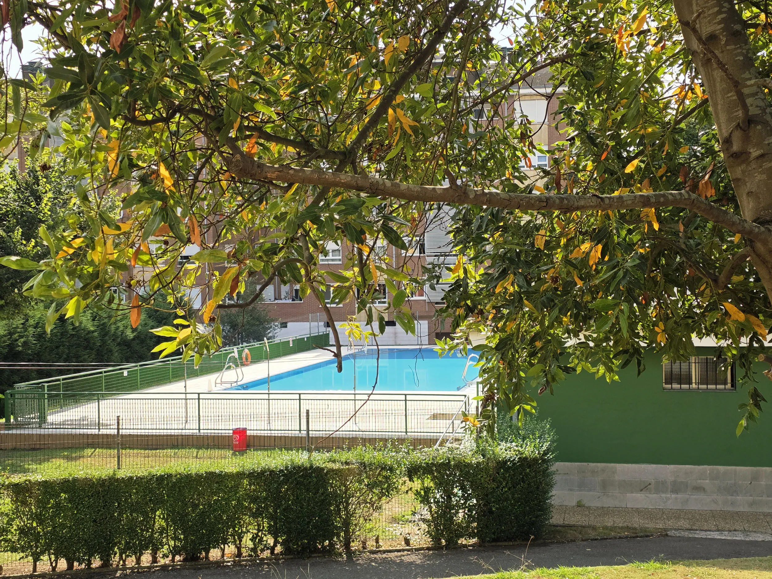 vista de las instalaciones desde el exterior. Edificio de servicios en primer plano y piscina detrás