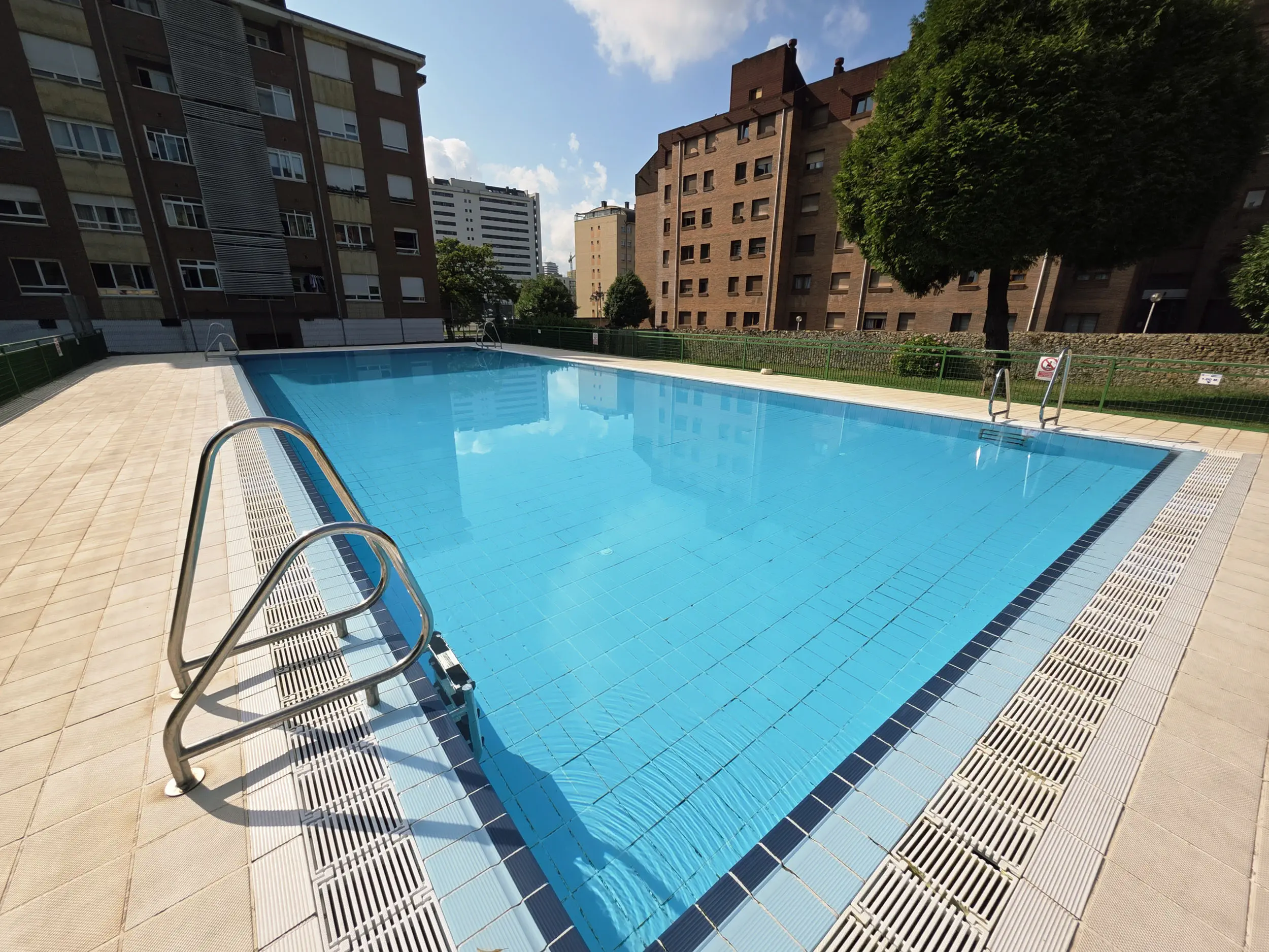 Vista de la piscina desde una esquina con edificios de viviendas al fondo