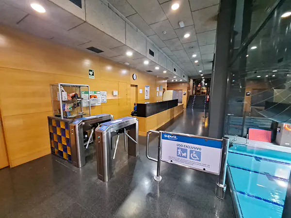 Tornos de control de acceso a las instalaciones interiores del centro deportivo, con el mostrador de recepción al fondo