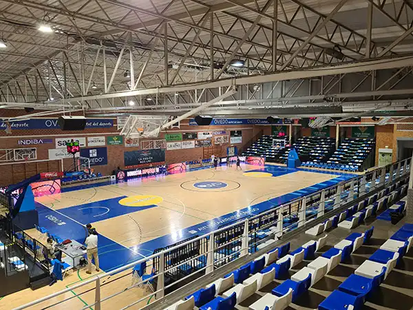 Pista central del polideportivo durante un partido de baloncesto. Gradas al fondo y en el lateral de la misma.