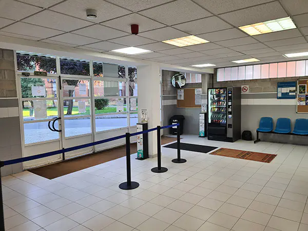 Puerta de entrada principal y recepción de la instalación donde hay una puerta acristalada y una maquina de vending