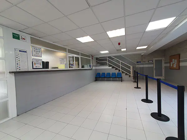 Hall de entrada a las instalaciones y recepción. Al fondo fila de bancos y escalera de acceso a la planta superior