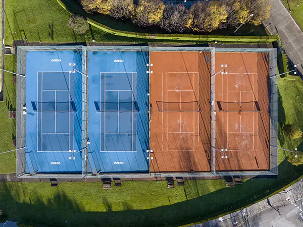 Vista cenital de cuatro pistas de tenis descubiertas. Dos de superficie Green Set y dos de tierra batida