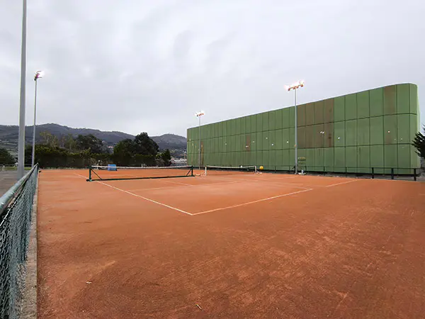 Dos pistas de tenis de tierra batida adosadas, con un edificio de instalaciones al fondo