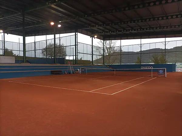 Vista general de una pista de tenis de tierra batida cubierta, con las gradas laterales y la cubierta
