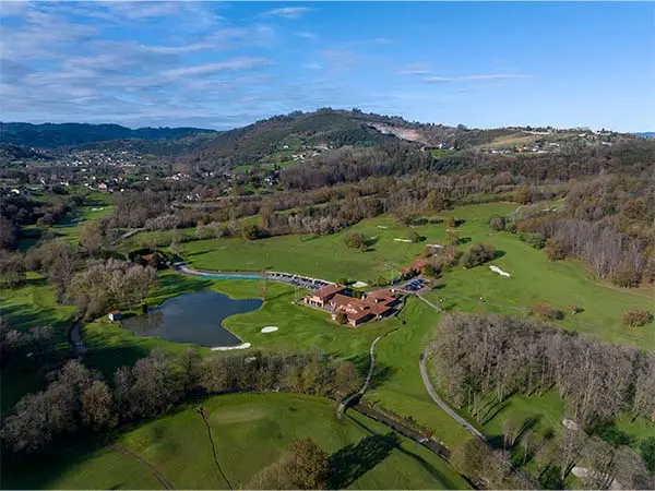 Vista aérea del campo de golf de Las Caldas, con grandes áreas verdes circundantes y un pequeño lago