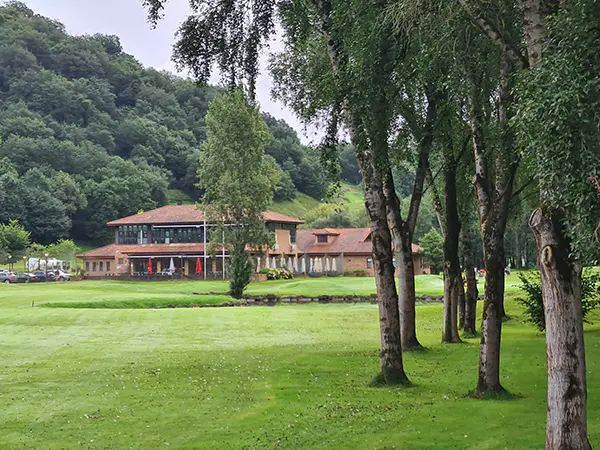 Edificio principal de visto desde los hoyos finales del campo en una zona con árboles y un lago