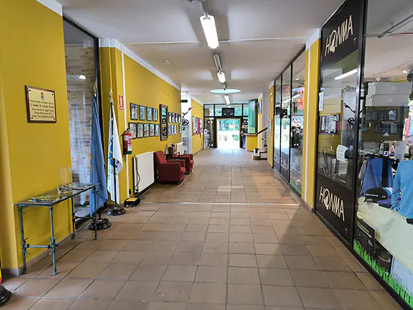 Pasillo interior, con escaparate de la tienda de artículos de golf. Al fondo, puerta de salida.