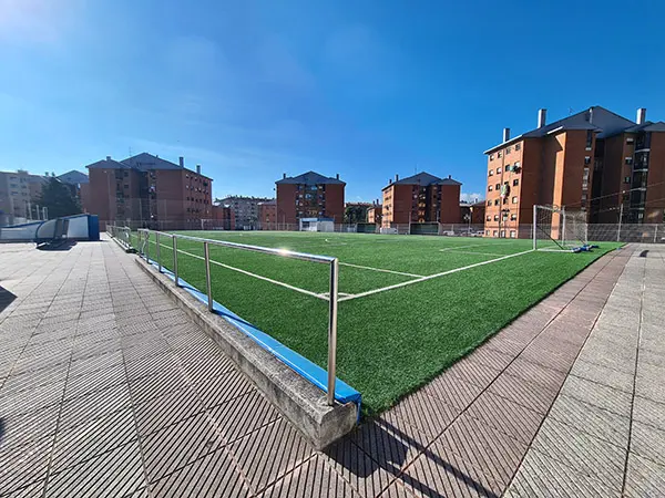 Exterior del terreno de juego. Se distinguen: una barandilla plateada, el césped, y la puerta de entrada a los vestuarios