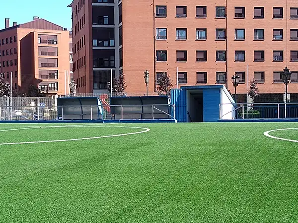 Zona de banquillos y puerta de entrada a vestuarios en color azul separada del césped por una barandilla plateada