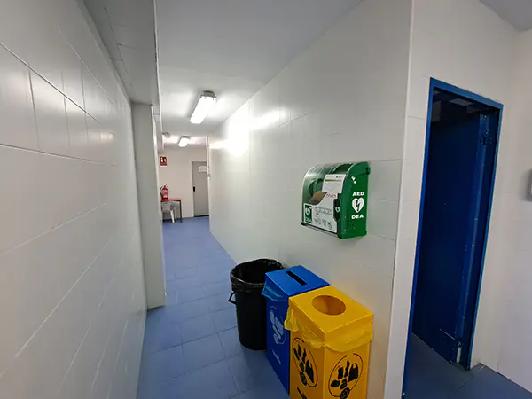 Pasillo donde se ubica la vitrina verde del desfibrilador y los cubos de reciclaje azul, amarillo y negro
