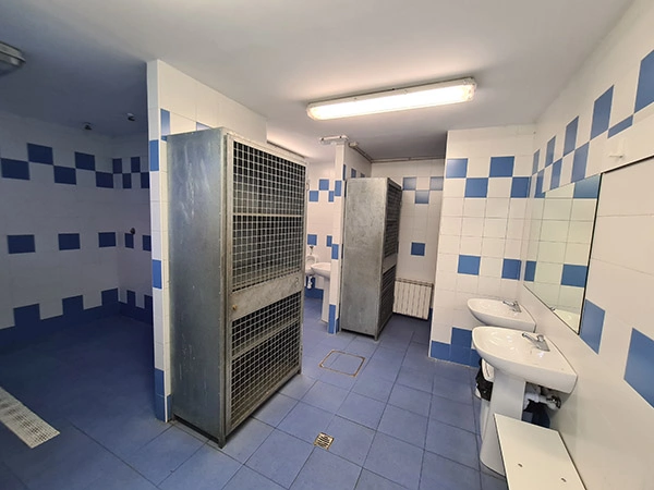 Baño con azulejos en blanco y azul distinguiéndose los lavabos, espejos y dos armarios enrejados de metal
