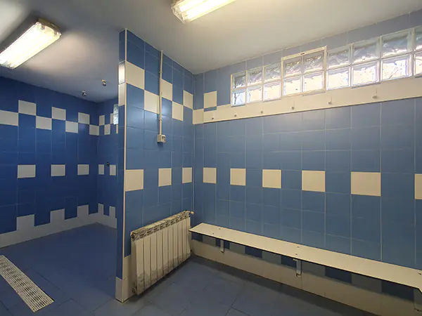 Zona de la ducha del vestuario de color azul y blanco, distinguiéndose un perchero y un banco en blanco