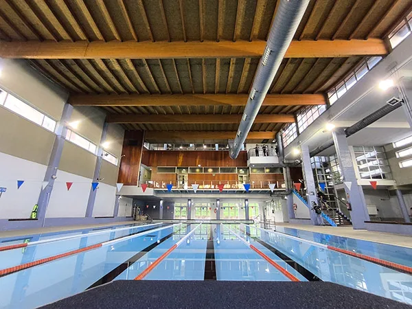 Vista a ras de suelo de la piscina climatizada, con detalle de la cubierta de madera y vista al fondo del piso superior