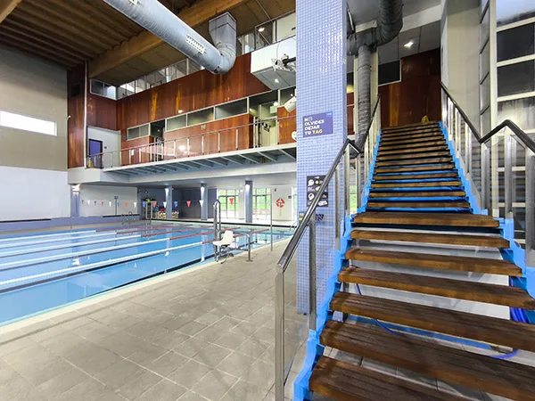Detalle de las escaleras de madera de acceso a las piscinas, con vista parcial de la piscina principal