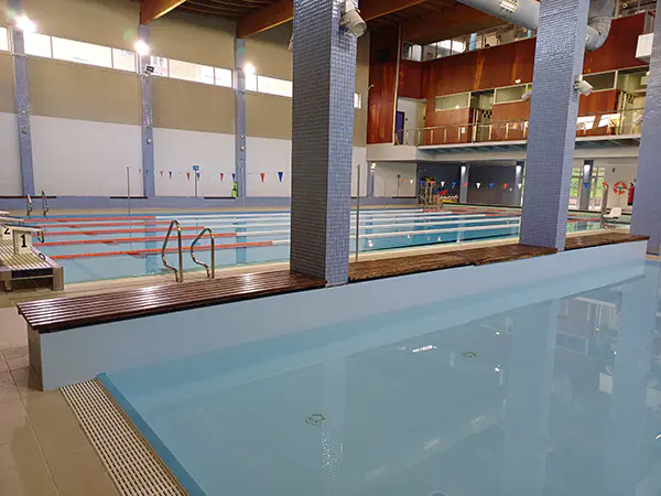 Vista de las piscinas, la de aprendizaje en primer plano y la de nado al fondo, con el banco de madera que las separa