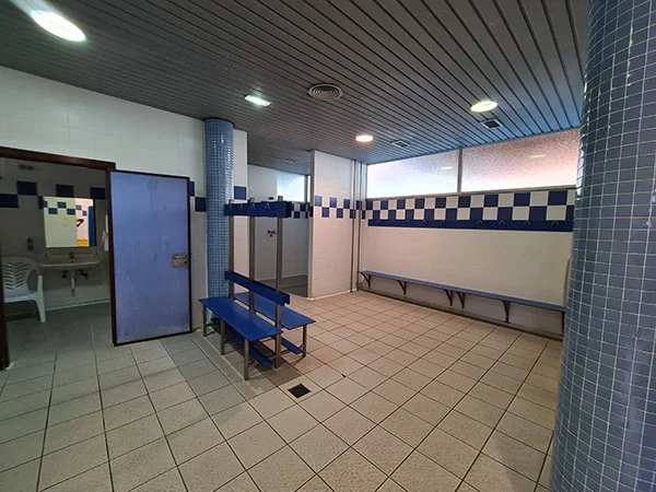 Vestuarios con bancos con perchas y una puerta abierta mostrando un lavabo