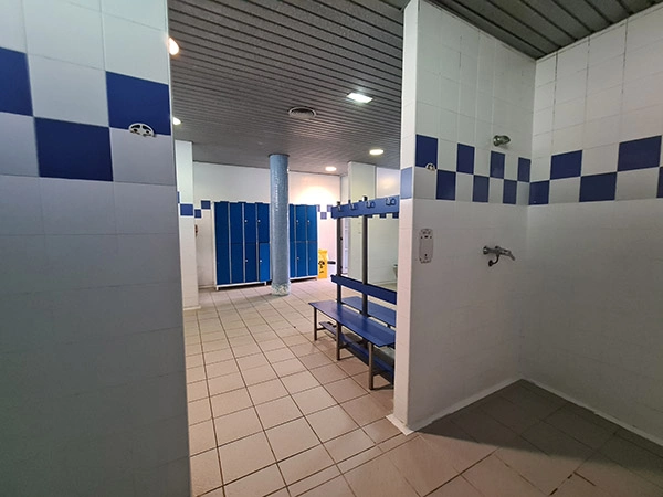 Vista de los vestuarios desde el área de las duchas, con bancos con perchas y taquillas
