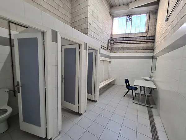 Interior de uno de los vestuarios, puertas de aseos, una mesa con silla, banco y perchas