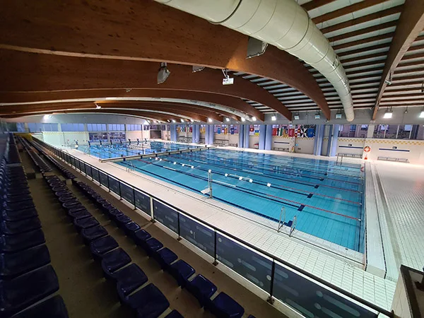 Panorámica de la piscina olímpica climatizada, con vistas del techo y parte de la grada, tomada desde la grada lateral