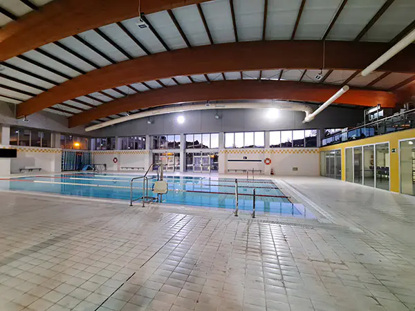 Vista lateral lejana de la piscina de aprendizaje, con detalle del suelo de azulejos y la barandilla de acceso
