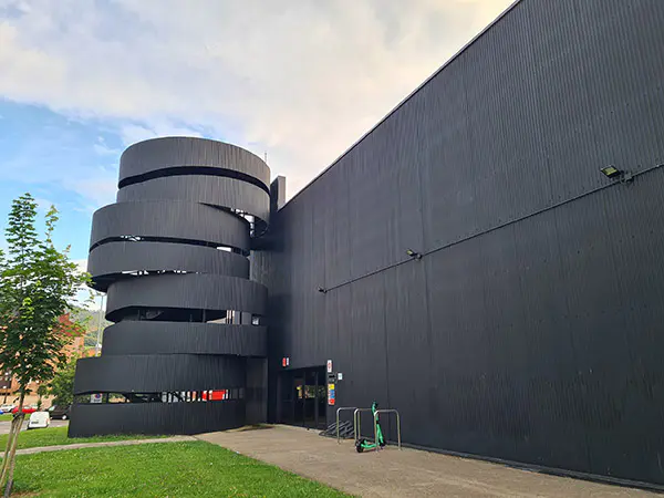 Vista exterior del edificio, con las escaleras exteriores, la puerta de entrada y un aparcamiento para patinetes eléctricos