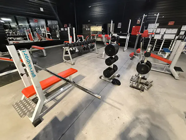Detalle de la sala polivalente 2, con espejo en un lateral, bancos de gimnasia, pesas y  máquinas de musculación