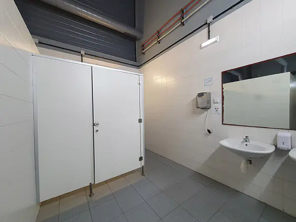Vista de los aseos, con baño adaptado a la izquierda. A la derecha, lavabo, espejo, dispensador de jabón y secador de manos.