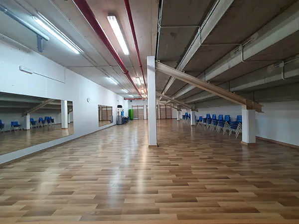 Sala polivalente bajo grada, vacía, con suelo de parqué y grandes espejos en un lateral