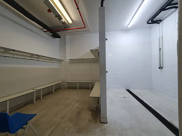 Vestuario, con bancos y perchas a la izquierda y zona de duchas a la derecha