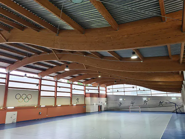 Panorámica de la pista polideportiva, con una portería y una canasta al fondo y una cubierta ondulada de vigas de madera
