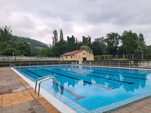 vista de la piscina con el edificio de servicios y las torres del castillo de Las Caldas al fondo