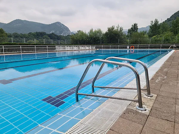 Vista de la piscina desde una esquina con escalera de acceso en primer plano