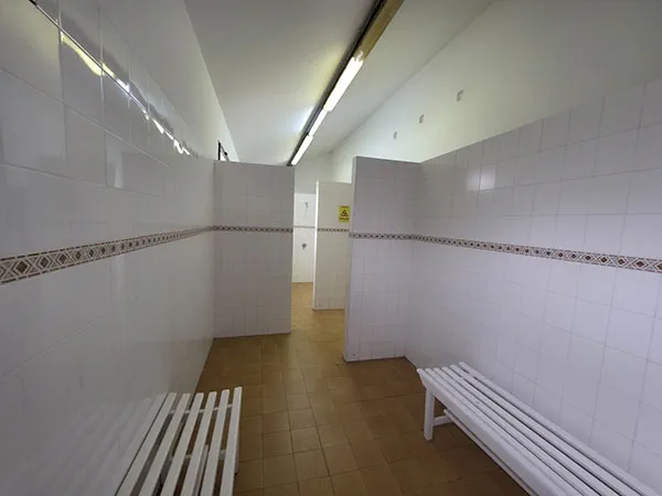 Zona de vestuario con bancos y primer plano y duchas al fondo