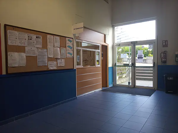 Puerta de acceso a las instalaciones y, junto a ella, una mostrador de información y un tablero de corcho con avisos
