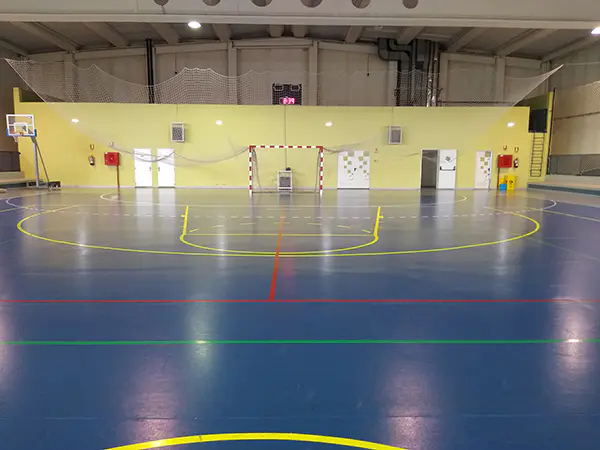 Vista en detalle del fondo de una pista polideportiva, con portería de fútbol, canastas portátiles y puertas de acceso