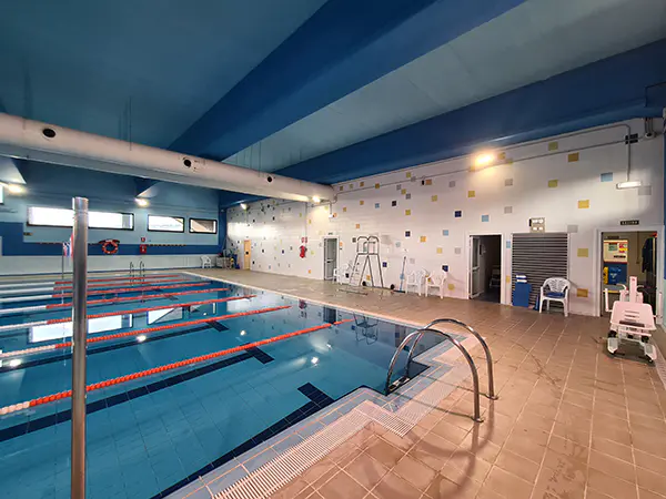 Vista lateral de la piscina principal, con barandillas de acceso, puerta de acceso al recinto y sillas