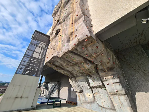Pared posterior del edificio, con un rocódromo adosado, escaleras acristaladas de acceso y una mesa de ping-pong