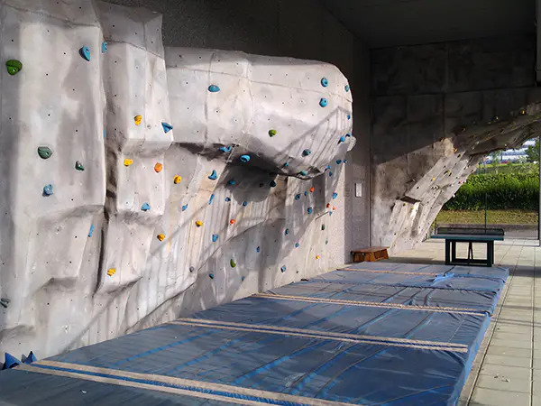 Vista en detalle del boulder, con colchonetas en el suelo y, al fondo, una mesa de ping-pong