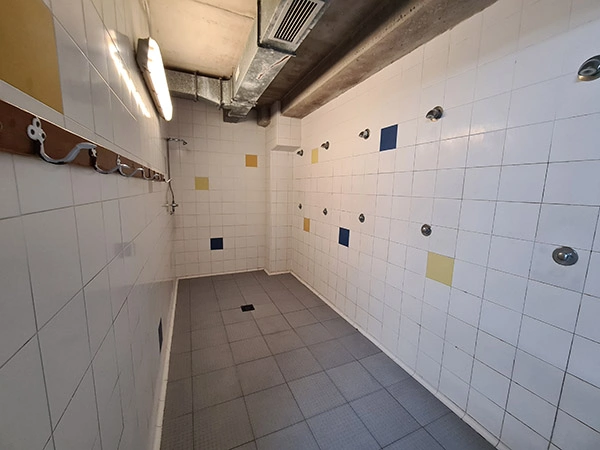 Pasillo de las duchas de los vestuarios, con paredes azulejadas y unas perchas en la pared de la izquierda