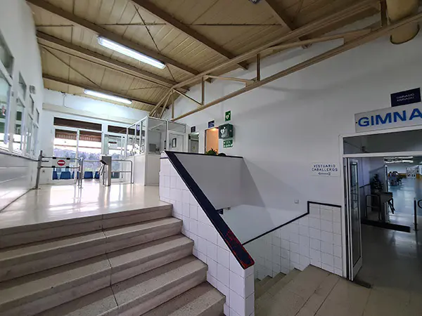 Vestíbulo de entrada, con escaleras de subida a la recepción y accesos al gimnasio y la zona de vestuarios