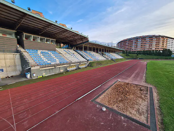 Vista lateral de las pistas de atletismo, con las gradas al fondo y detalle de la zona de saltos