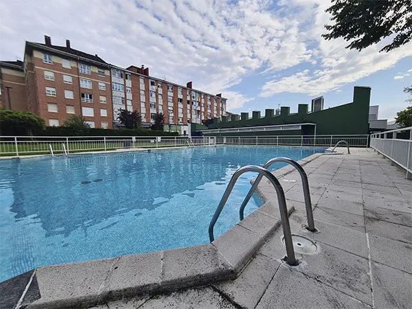 vista del vaso de la piscina con el edificio de servicios y un edificio de viviendas al fondo