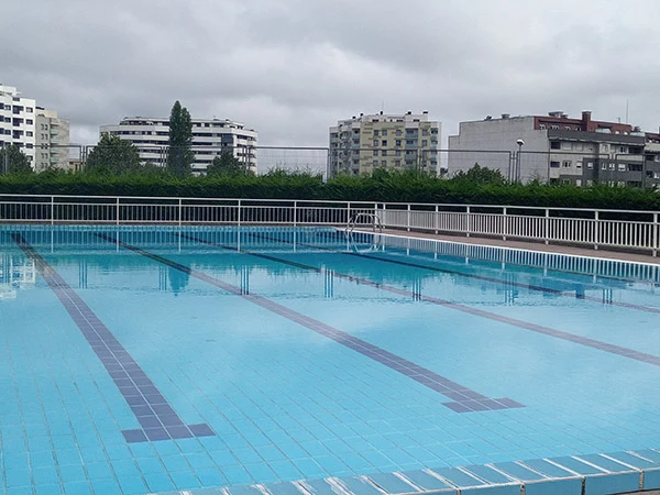 Vista parcial de la piscina principal, con las vallas perimetrales y edificios circundantes al fondo